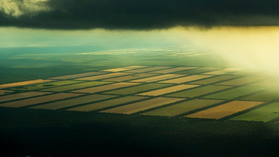 An aerial photo showing rectangular sections of land with dark clouds overhead and a dark foreground.