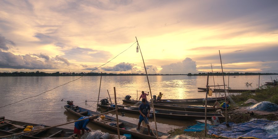 Fishermen outfit their long skinny boats with nets on the bank of a river at sunrise