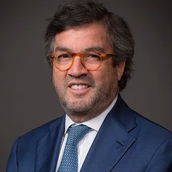 Headshot of Luis smiling. He is wearing a blue suit and has brown glasses on.