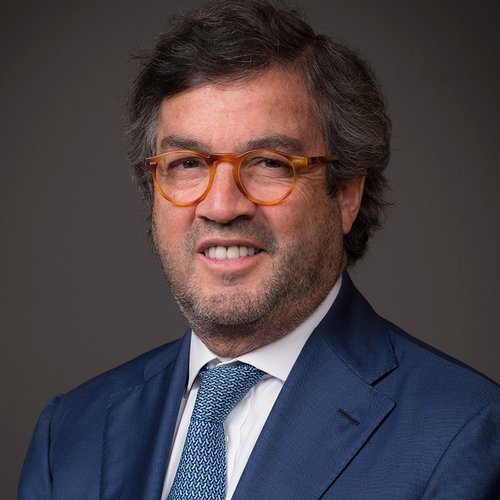 Headshot of Luis smiling. He is wearing a blue suit and has brown glasses on.