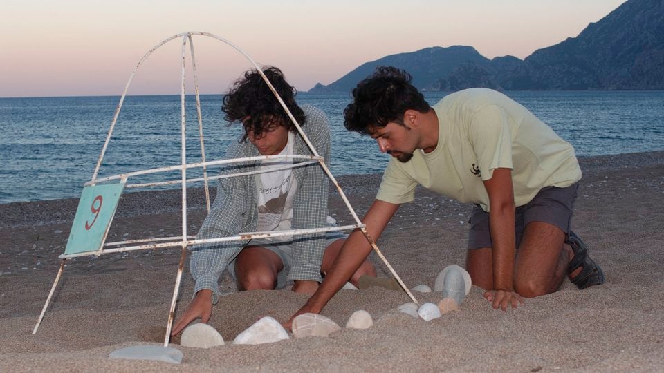 Two people arranging rocks on a beach around a metal loggerhead turtle nesting tent.