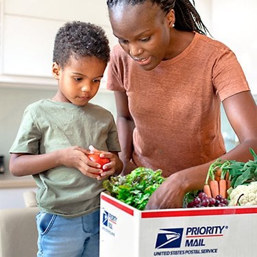 Woman and child opening USPS box full of vegetables