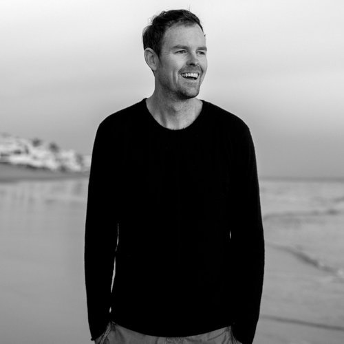 A black and white photo of Thomas McInerney standing on a beach and smiling while looking to the right side of the frame