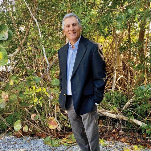 Sanjeev Mehra standing for a headshot with plants in the background