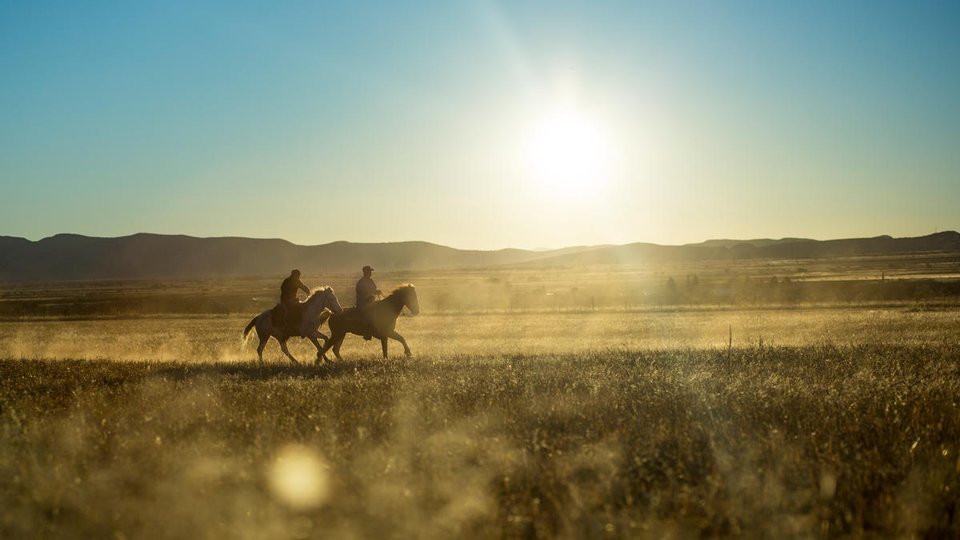 Father and son of ejido farm community ride their horses at sunset.