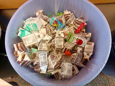 A top down view of empty school milk cartons in a trash can.