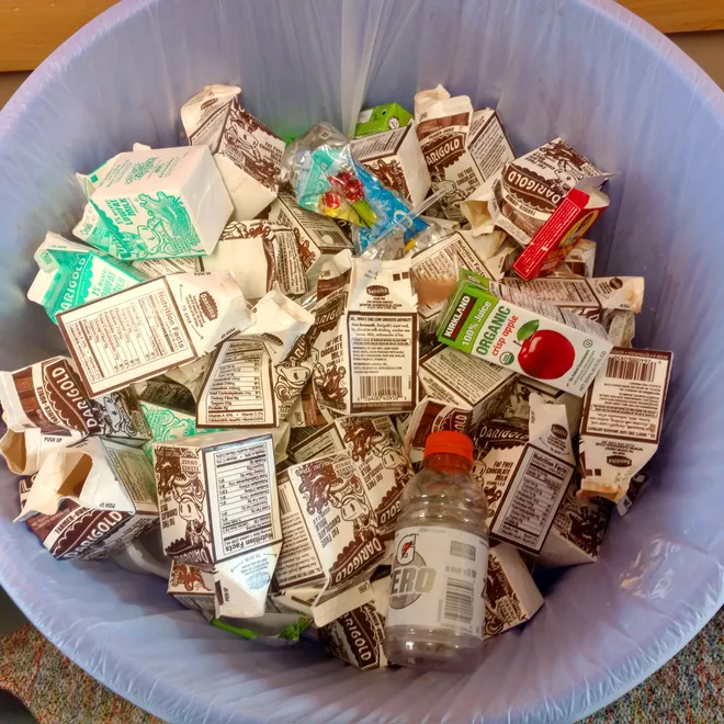 A top down view of empty school milk cartons in a trash can.