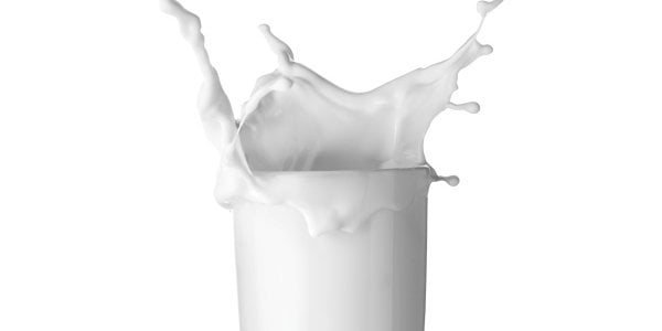 A clear glass filled with white milk splashing upward from the top of the glass.