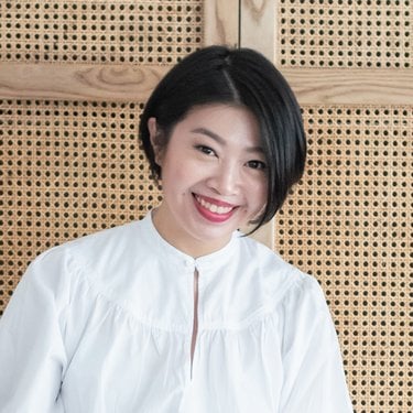 A head shot of a woman with a black bob, red lipstick and a white blouse.