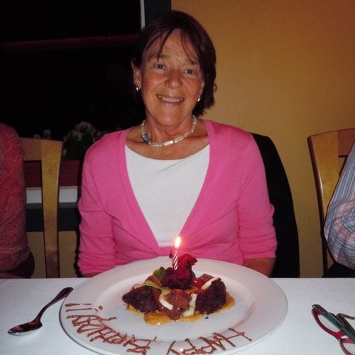A photo of a smiling woman sitting at a table in front of a piece of cake