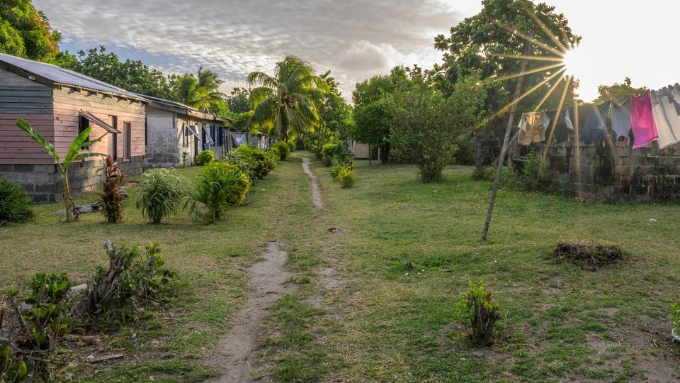 Sun breaks through view of homes and clothesline in Nacula Village, Yasawa Islands, Fiji