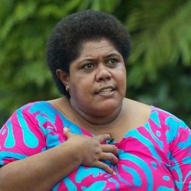 Lavenia Naivalu, wearing a brightly colored top, holds her hand to her chest as she speaks