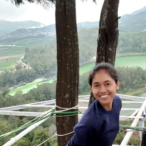 Nety Riana Sari stands beside a tree overlooking a forest and smiles at the camera