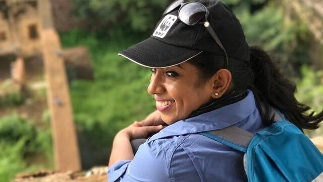 A color photo showing a woman with a baseball hat with the WWF panda logo looking back at the camera outside