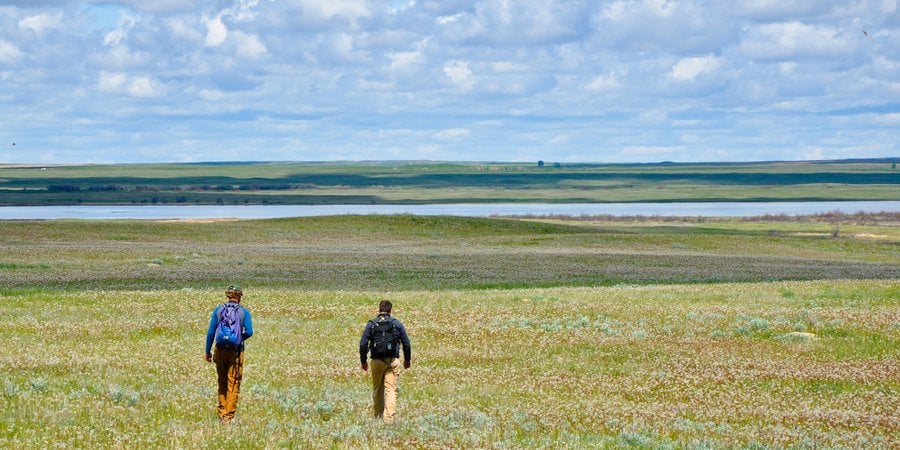 Two people walk away into the distance of a vast horizon of the Northern Great Plains.