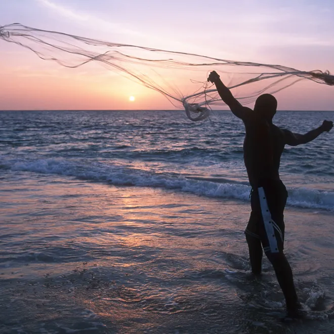 A fisherman casts his fishing net on the coast at sunset Gabon