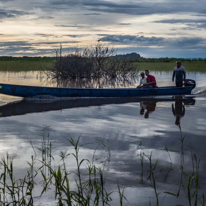 A thin canoe at the center of a photo of a waterway with marshlands around it