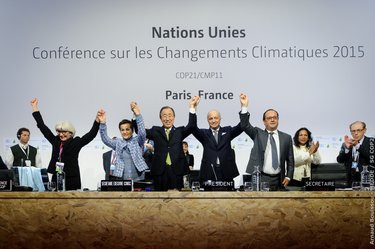 A color photo showing a diverse group of leaders holding hands triumphantly above their heads at a conference. The conference name is on the wall behind them in French.