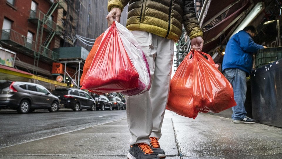 A pedestrian carries two red plastic bags through a city street