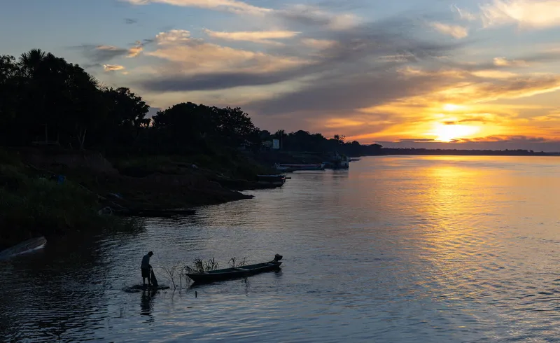 A person stands near a canoe in dwindling light on a river