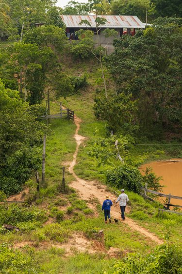 Two people and a dog walk a path toward a ranch building