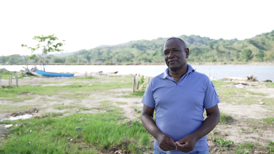Portrait of Jesús Antonio Julio Cuestas in a blue shirt in front of a body of water on a sunny day