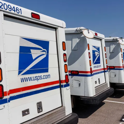 A row of US Postal trucks lined up in a parking lot