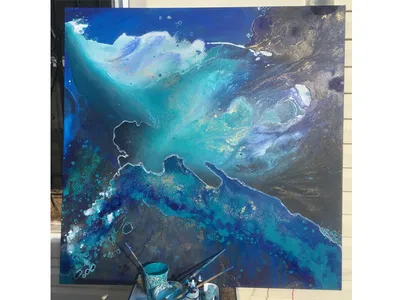 A painted canvas of an abstract ocean is propped up on a seat. In front of it is a tray of brushes and paints.