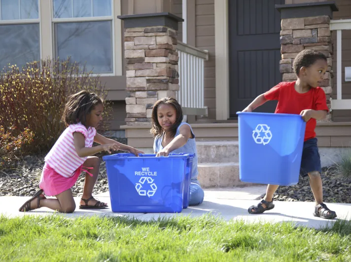 Children place items in recycling bins in front of a house