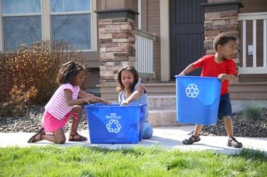 Children place items in recycling bins in front of a house
