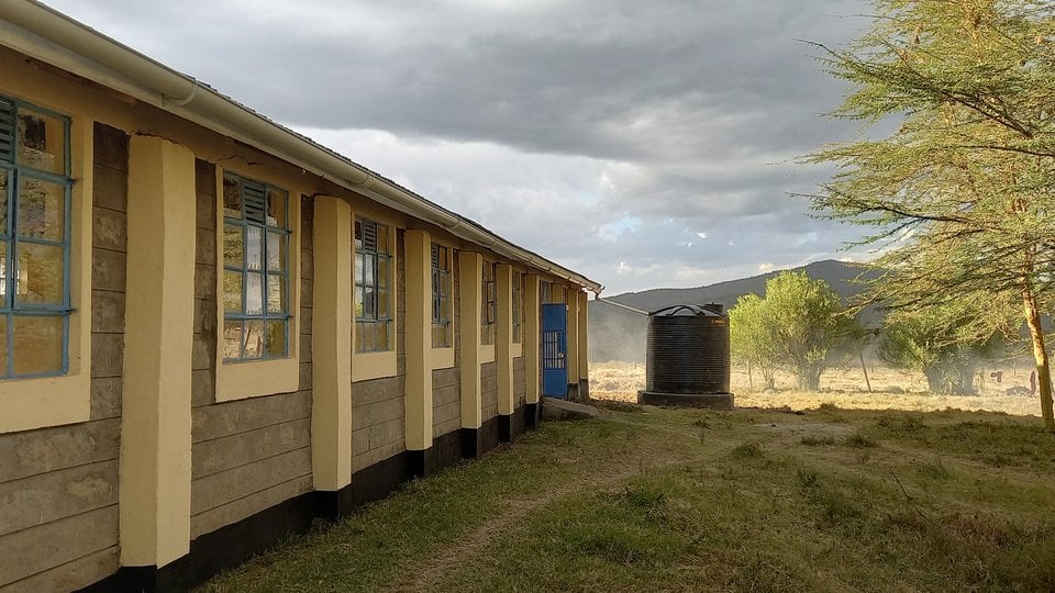In the foreground are a school building and rainwater harvesting system. In the background is a mountain. The sky is grey.