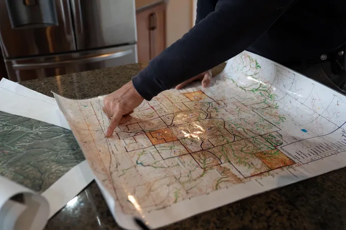 A rancher points at a map sitting on a countertop
