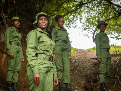 Four female rangers in green uniforms stand on a wooded trail