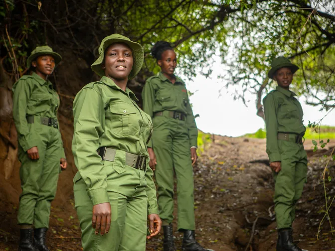 Four female rangers in green uniforms stand on a wooded trail