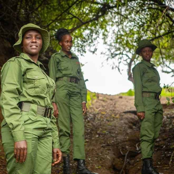 Four female rangers in green uniforms stand on a wooded trail