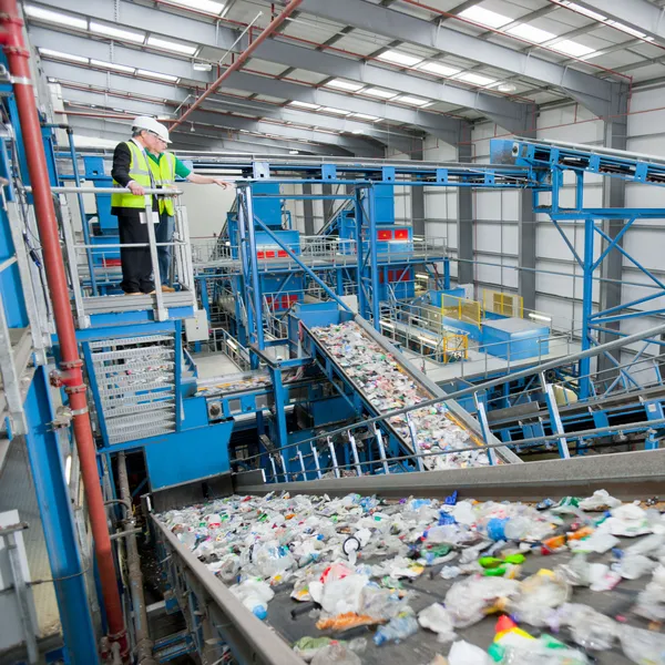 Two people stand on an elevated walkway overlooking a recycling plant