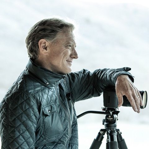 A photo of a man smiling next to a large professional camera