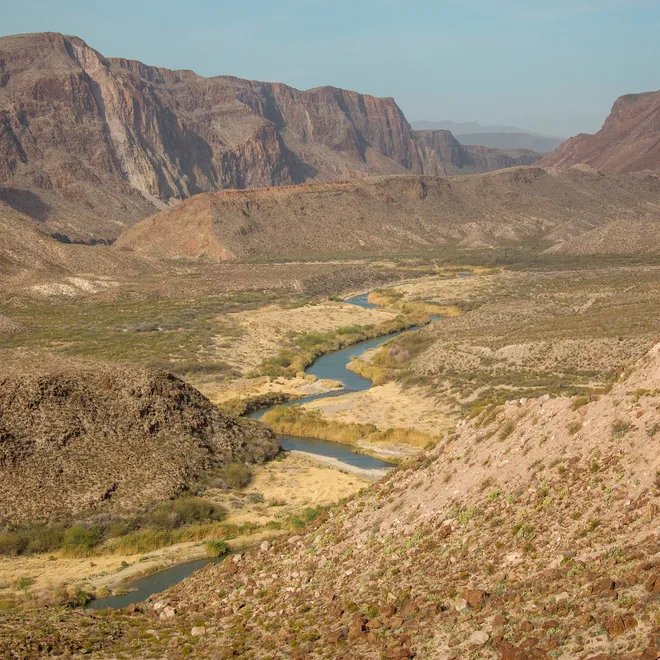 A landscape photo  with brown mountains in the background and a river in a valley at the center.