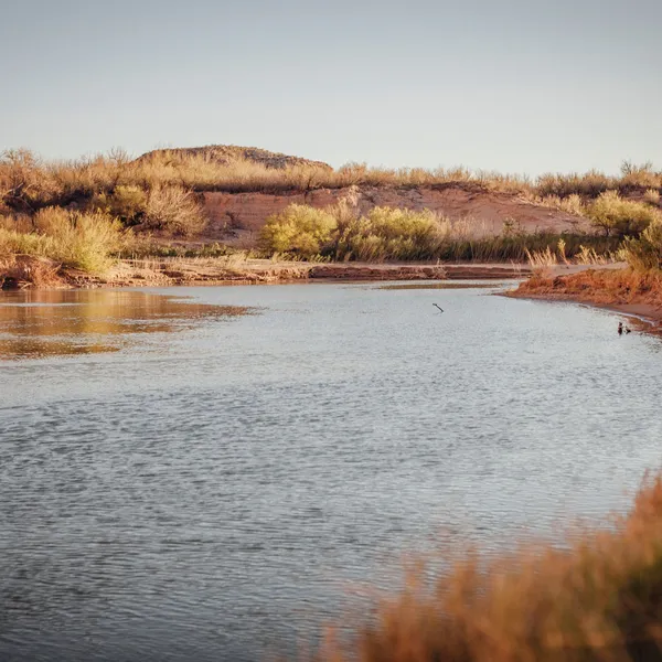 A calm stretch of river in dimming light with desert shoreline and blue sky