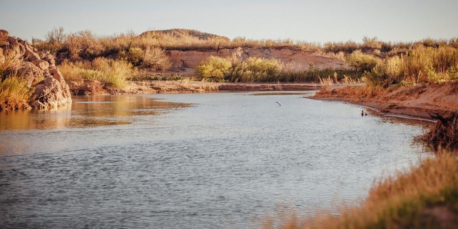 A calm stretch of river in dimming light with desert shoreline and blue sky