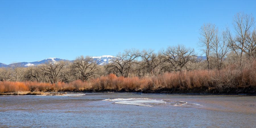 A wide river flows amid a backdrop of trees and mountains