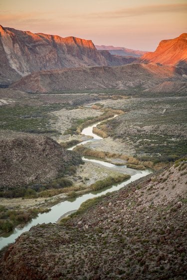 A river winds through a reddish-brown canyon as the sun sets