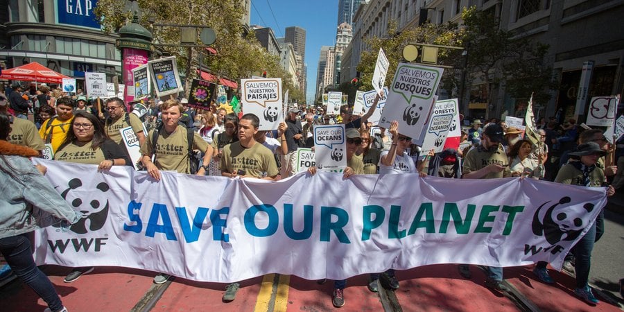 People march behind a sign that reads 'save our planet' on a sunny day in San Francisco