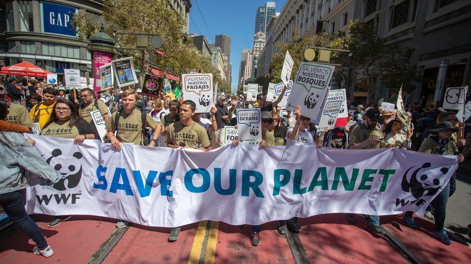 People march behind a sign that reads 'save our planet' on a sunny day in San Francisco