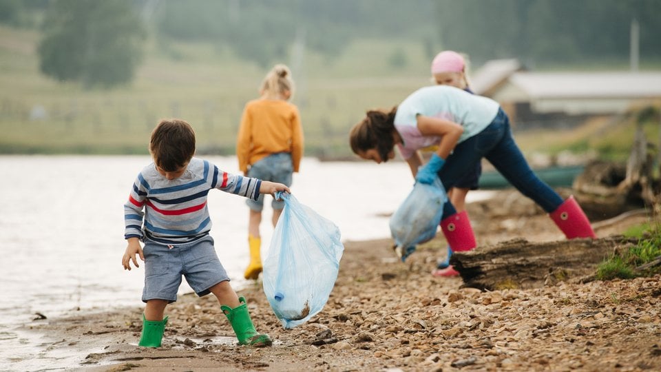 A group of people along a river bank clean up trash and put it in a trash back