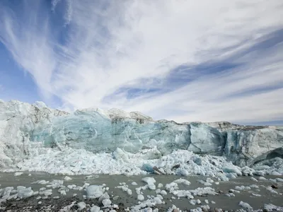 An icy blue glacier with chunks of ice in the water and blue skies with white clouds.
