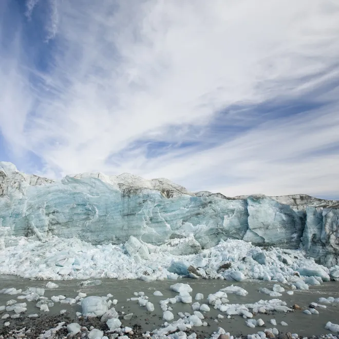 An icy blue glacier with chunks of ice in the water and blue skies with white clouds.
