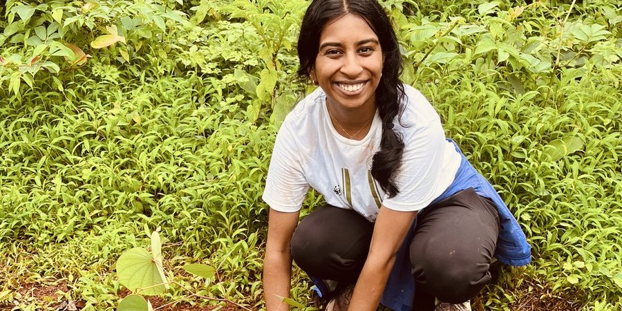 Sanjana Ramesh looks up at the camera while planting a plant in the soil