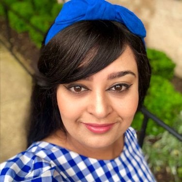 The head shot of a woman with dark hair and a blue and white gingham top.