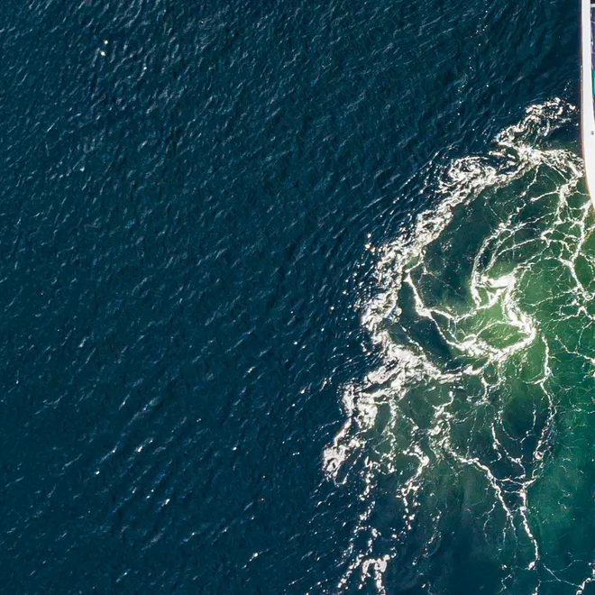 Aerial photo of ship on blue ocean with green swirls in wake